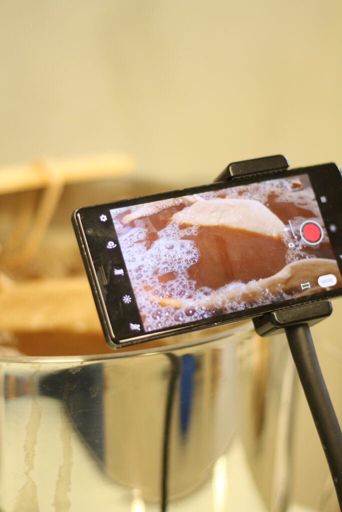 Téléphone filmant un bain de symplocos pour préparer le tissu à la teinture végétale. Bain de couleur marron avec des bulles et du textile écru car non teint à cette du processus